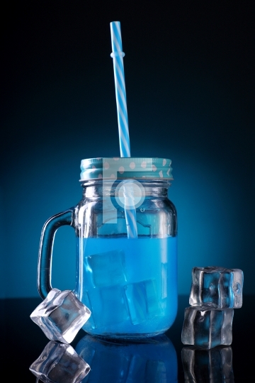 Blue Colored Cocktail in a Mason Jar with Straw and Ice Cubes
