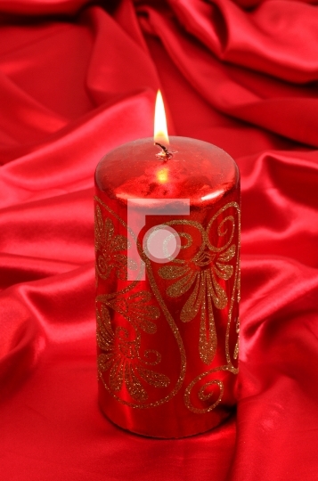 burning red colored candle with glitters on satin background