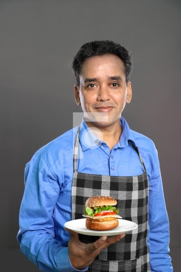 Indian Male Chef with a Burger in Hand on Grey Background