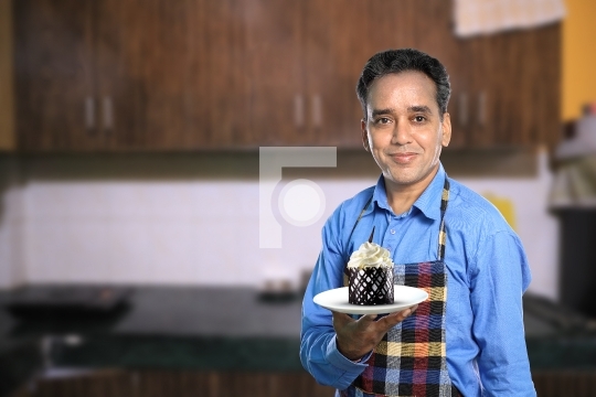 Indian Male Chef with a Sweet Cake with Kitchen Interiors