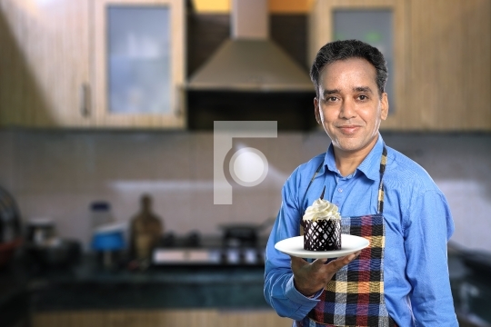 Indian Male Chef with a Sweet Cake with Kitchen Interiors
