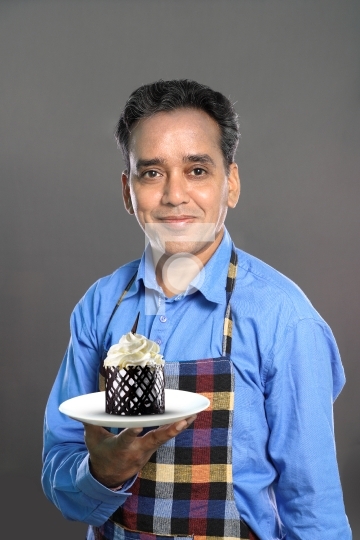 Indian Male Chef with a Sweet Dish Cake on grey Background