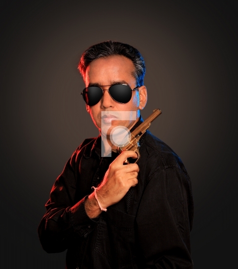 Indian Man with sunglasses and gun on dark background