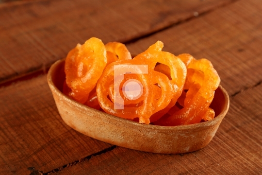 Indian Sweet Jalebi in a handmade pottery bowl on wooden backgro