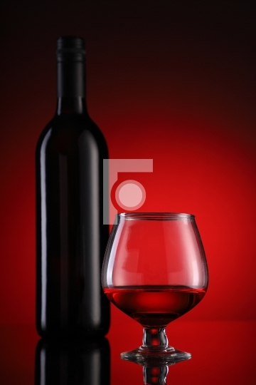 Red wine glass and bottle on red background