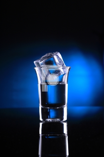 Shot Glass with an Ice Cube on Blue background